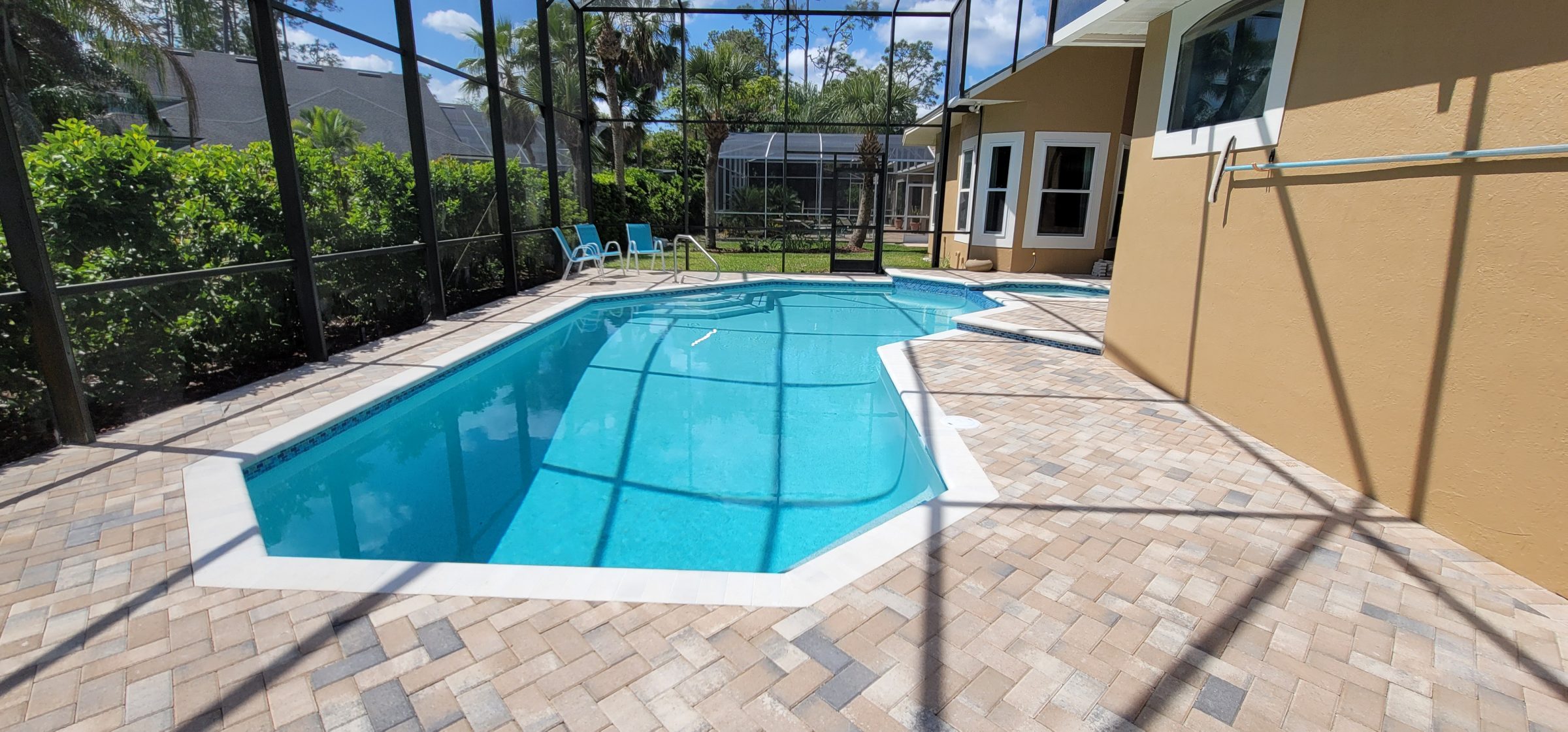 Outdoor pool with screened enclosure and chairs.